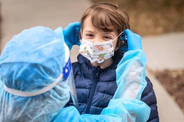 Female nurse adjusting a protective face mask to a child after performing a Covid-19 test on him before going back to school stock photo