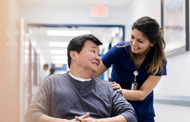 De aide van de vrouwelijke verpleegster glimlacht bij rijpe mannelijke patiënt in rolstoel​​​ foto