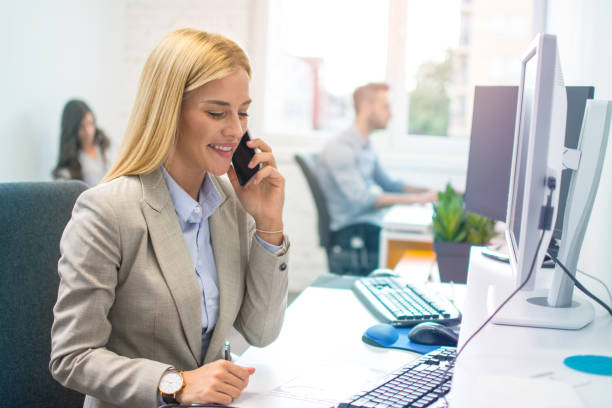 Female office worker in formalwear talking on mobile phone at office workplace stock photo