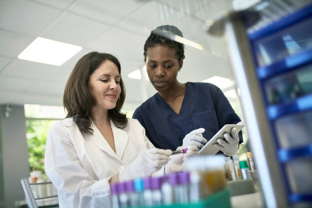 Female Pathologist and Technician Examining Test Tube Sample Low angle close-up of smiling Hispanic female pathologist and technician with digital tablet examining test tube blood sample. immunology stock pictures, royalty-free photos & images