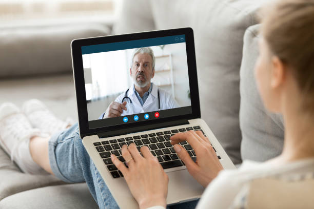 Female patient consult with doctor online using video call Young woman sit on couch at home have video call with doctor use wireless internet connection on laptop, female patient talk consult with physician online on webcam conference on computer nurse talking to camera stock pictures, royalty-free photos & images