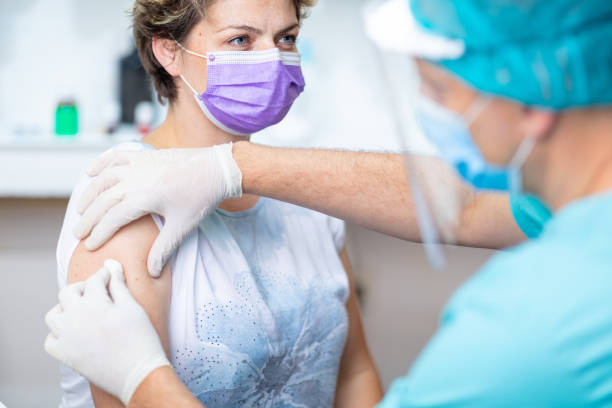Female patient's arm disinfected with cotton pad for vaccination Female patient with protective face mask waiting for vaccination, doctor in surgical gloves disinfecting her arm preventative medicine stock pictures, royalty-free photos & images
