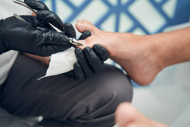 Female pedicure specialist cutting cuticle on male toe Close up of woman hands in sterile gloves using stainless steel scissors while doing pedicure for male client man pedicure stock pictures, royalty-free photos & images