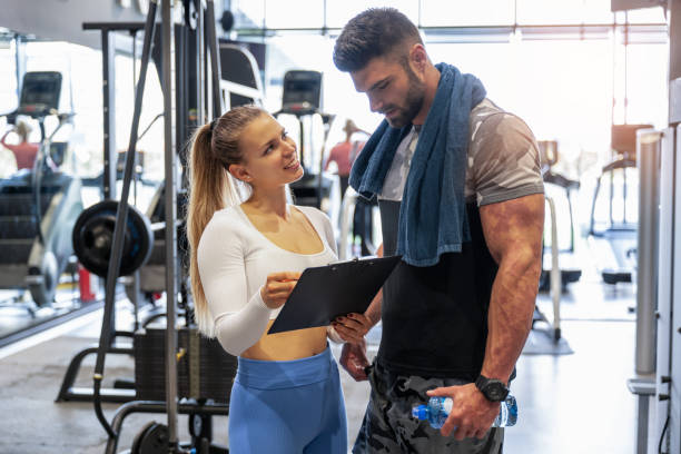 Female personal trainer showing exercise progress to her male client in a gym. stock photo