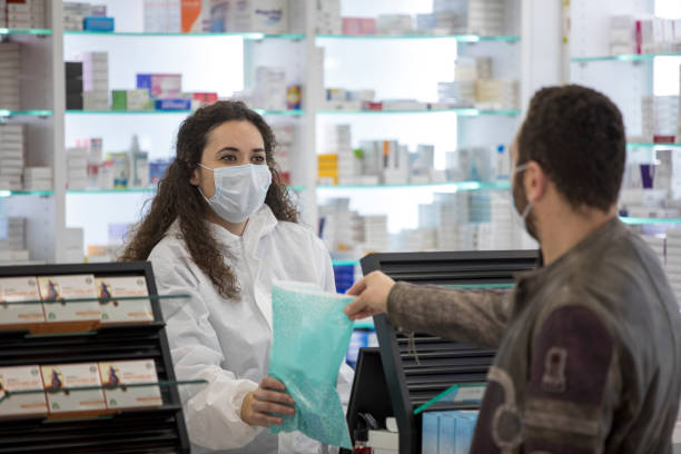 외과 용 마스크를 착용한 여성 약사가 환자에게 약을 제공합니다. - pharmacy 뉴스 사진 이미지
