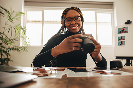 Female photographer holding a dslr camera in her home office. Happy young woman smiling at the camera while working at her desk. Creative female freelancer working on a new project.