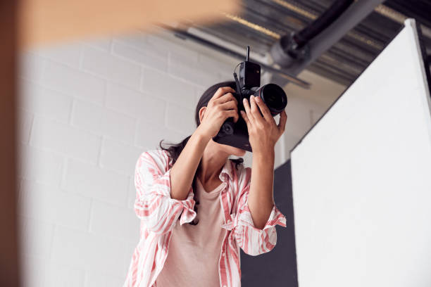 photographe féminin avec l'appareil-photo sur la séance photo contre la toile de fond blanche de studio - photographe professionnel photos et images de collection