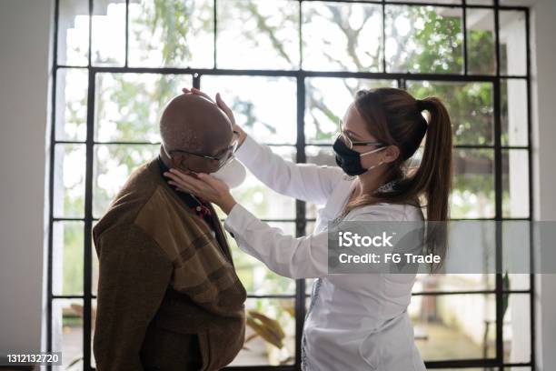 Female physical therapist assisting senior patient at home - wearing face mask