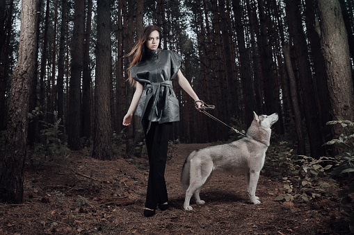 Female portrait of woman outdoors in the forest with wild dog together. Fairy tale atmosphere in dark. Fashion people. Woodland dweller in the nature. Friendship of human and animal like a wolf