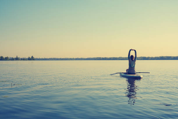 Female practicing yoga on a SUP board during sunny morning stock photo