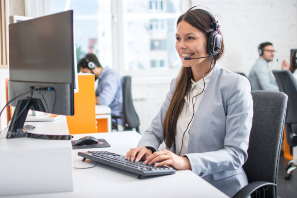 Female professional call center telesales agent wear wireless headset using computer in customer care support service office with team. stock photo