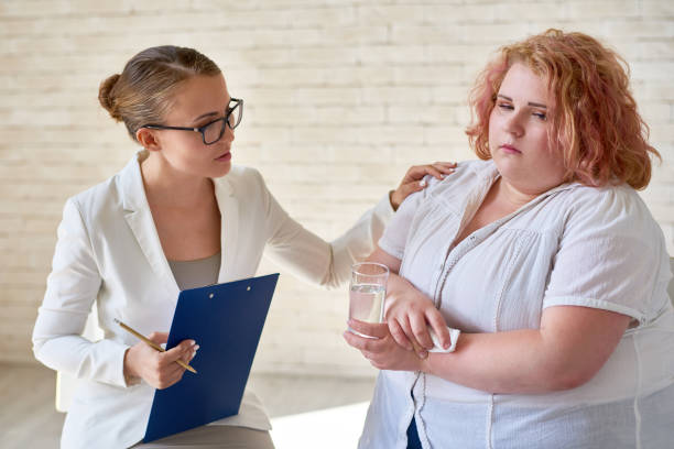 Female Psychiatrist Comforting Crying Patient Portrait of beautiful young woman  comforting  crying obese woman during therapy session on mental issues obesity stock pictures, royalty-free photos & images