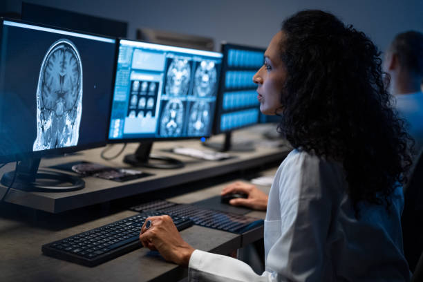 Female radiologist analysing the MRI image of the head Side view of female radiologist looking at the MRI image of the head on her monitor and analysing it. medical scan stock pictures, royalty-free photos & images