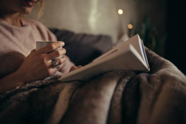 female reading book on bed at night - ler imagens e fotografias de stock