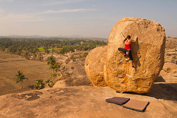 female rock climber scaling boulder on top of mountain - hampi stockfoto's en -beelden