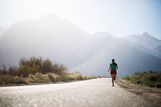 female running Female athlete, endurance running on a endless road with mountains in the back ground  vanishing point stock pictures, royalty-free photos & images