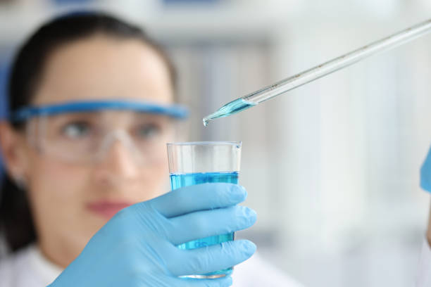 Female scientist dripping and pipetting into flask of blue liquid stock photo