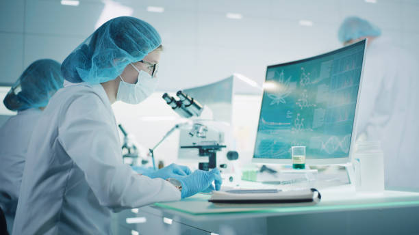 Female scientist testing medical marijuana, making notes. Team working in background. Charts and models on computer screens. Modern laboratory interior stock photo