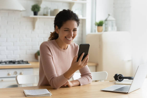 Female sit indoor holding modern smartphone laughing at online video stock photo