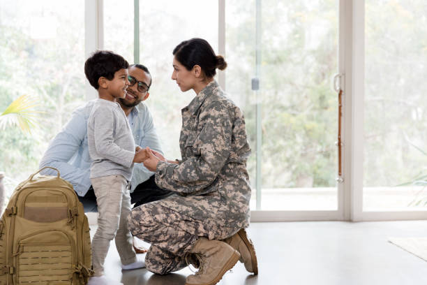Female soldier tells family goodbye before deployment A mid adult female soldier kneels down and holds her young son's hands while speaking sweetly to him. She is preparing to leave for a long deployment. soldiers returning home stock pictures, royalty-free photos & images