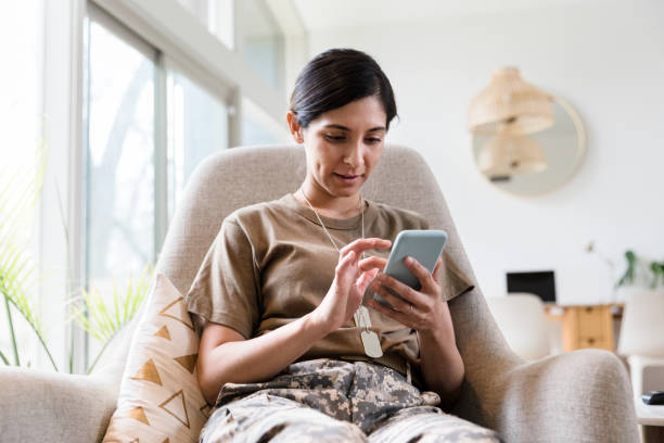 Female soldier texts while relaxing at home Mid adult female soldier concentrates while using a smartphone while relaxing in her home. military lifestyle stock pictures, royalty-free photos & images