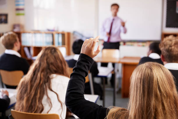 female student raising hand to ask question in classroom - school imagens e fotografias de stock