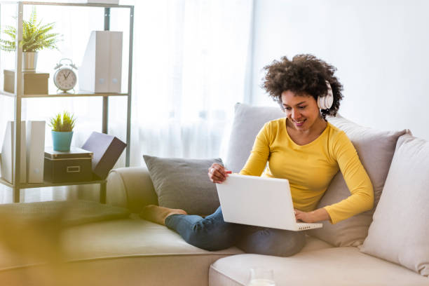 Female studying at home Young beautiful African american woman relaxing and listening to music using headphones. Smiling young woman watching a video with her laptop while siting on a sofa free images for downloads stock pictures, royalty-free photos & images