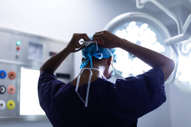 Female surgeon wearing surgical mask in operation theater at hospital Rear view of Mixed-race female surgeon wearing surgical mask in operation theater at hospital surgeon stock pictures, royalty-free photos & images