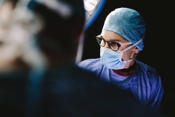 Female surgeon with team performing surgery Surgeon wearing medical mask with medical team performing surgery in hospital operation theater. surgeon stock pictures, royalty-free photos & images