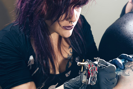 Female Tattoo Artist Works On A Tattoo Stock Photo - Download Image Now