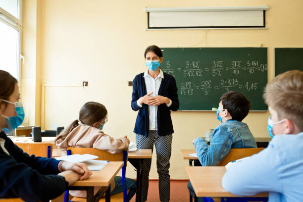 Female teacher teaching mathematics at school during Covid-19 Female teacher wearing N95 Face masks teaching mathematics at high school. Back view of students sitting at desks in the classroom. british curriculum schools stock pictures, royalty-free photos & images