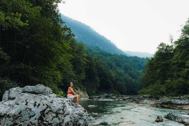 Female traveler sitting on the rock inside the scenic mountain canyon in Montenegro Young woman in red swimsuit exploring the Balkans, enjoying summer sunset in the canyon with mountain view at Durmitor National park women in skimpy bathing suits stock pictures, royalty-free photos & images