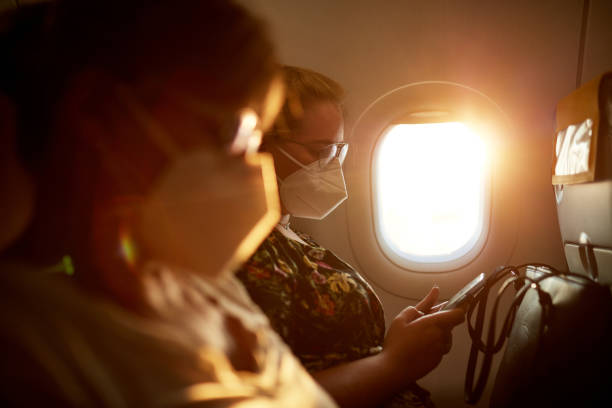 Female Travelers Wearing KN95 Masks on Airplane Side view with focus on background of mature Caucasian mother and teenage daughter wearing protective masks as they travel by airplane in time of COVID-19. plane window seat stock pictures, royalty-free photos & images
