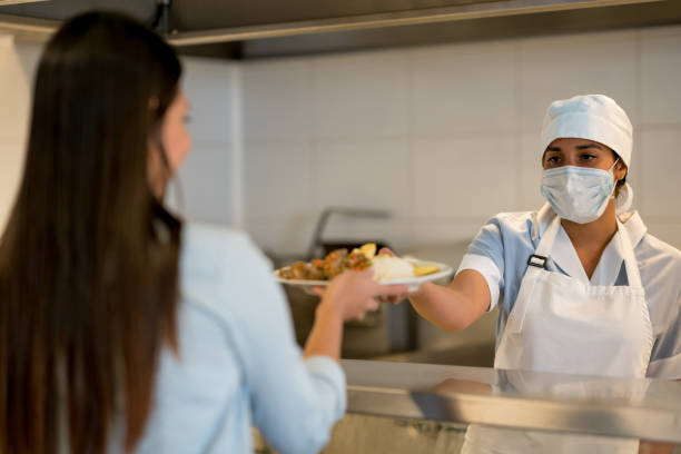 Female worker at a buffet restaurant handing the plate with food to customer Female worker at a buffet restaurant handing the plate with food to female customer cafeteria stock pictures, royalty-free photos & images