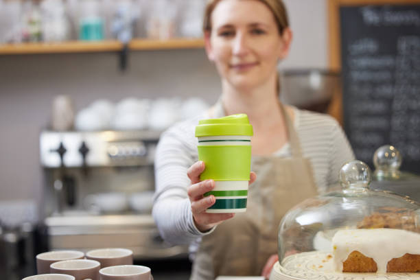 Female Worker in Cafe Serving Coffee In Sustainable Reusable Cup stock photo