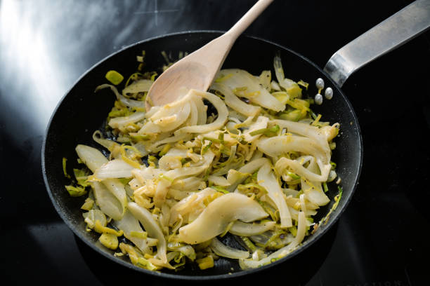 Fennel slices and leek in a black frying pan on the stove, cooking vegetarian with healthy vegetables stock photo