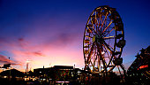 istock Ferris Wheel at Sunset with electric lights and carnival games and Rides in Image Purple and Pink Sunset 1320998575