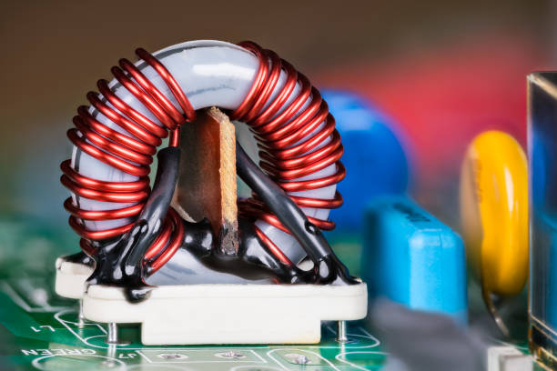 Ferrite core inductor on white holder and colored capacitors on a green circuit board stock photo