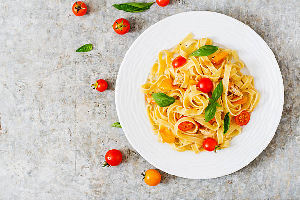 Fettuccine pasta in tomato sauce with chicken, tomatoes Fettuccine pasta in tomato sauce with chicken, tomatoes decorated with basil on a table. Top view tagliatelle stock pictures, royalty-free photos & images