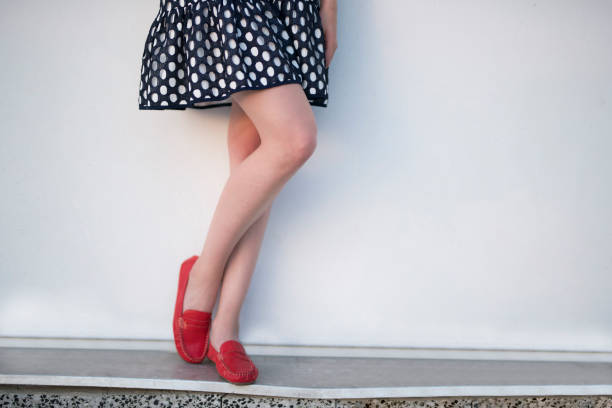 Fashion portrait of unrecognizable, young woman in dotted spring dress and red moccasin, standing against the wall and posing; cut out