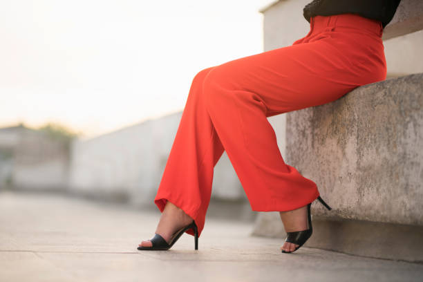 Fashion portrait of an unrecognizable young woman sitting at the balcony in red trousers and high heels; cut out.