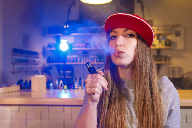 kuvapankkikuvat ja rojaltivapaat kuvat aiheesta nuori kaunis nainen punaisessa lakissa polttaa sähkösavukkeen höyrykaupassa - vape shop prank