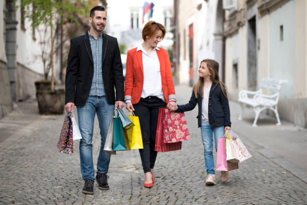 Young couple with adorable little girl, age 8, walking in an old city with bunch of shopping bags. They are holding their hands, the girl is in on the right and they are smiling.