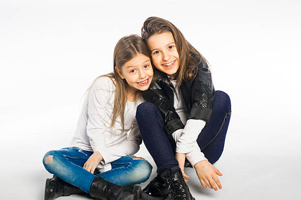 Studio shot of two little sisters posing on the floor and looking at camera.