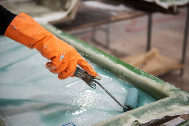 Fibreglass factory worker rolling solution on fibreglass sheets Hand of a fiberglass factory worker in an orange rubber glove rolling solution on fiberglass sheet fibreglass stock pictures, royalty-free photos & images