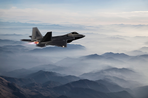 F-22 fighter jet flying over fogy  mountains at dusk