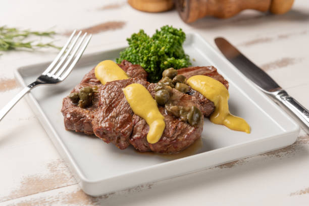 Filet mignon with caper and mustard sauce, broccoli, pepper grinder on wooden white background, soft light stock photo