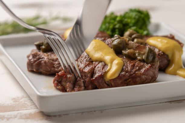 Filet mignon with caper and mustard sauce, broccoli, pepper grinder on wooden white background, soft light stock photo