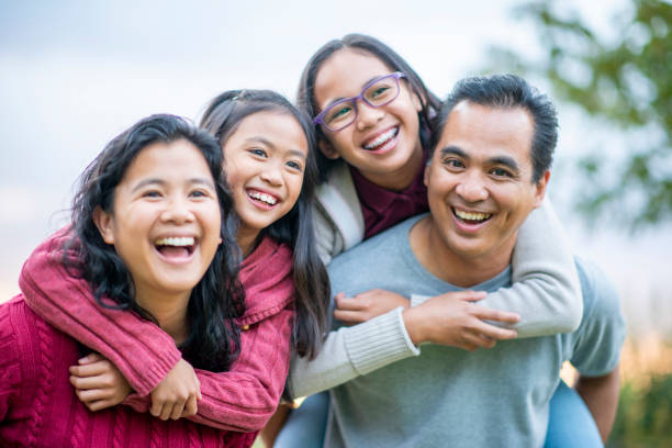 Filipino Family Laughing Piggyback Portrait stock photo A small Filipino family of four spend some time close together while outside.  The Mother and Father each have an elementary school aged daughter on their back and they are laughing and enjoying a walk in the fresh air. filipino family stock pictures, royalty-free photos & images