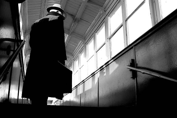 Film Noir style man Film Noir style gangster or detective ,man is wearing a fedora hat and trench coat, he is carrying a suitcase. gangster stock pictures, royalty-free photos & images
